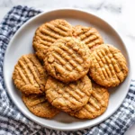 A plate of freshly baked almond flour peanut butter cookies with a classic crisscross pattern.